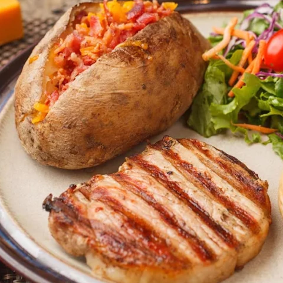 Charbroiled steak with a loaded baked potato and a side salad on a plate.