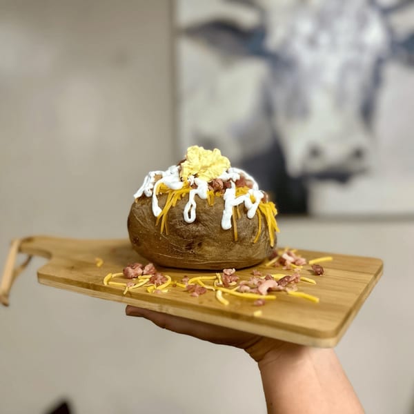 A loaded baked potato with butter, sour cream, cheese, and bacon bits on a wooden board.