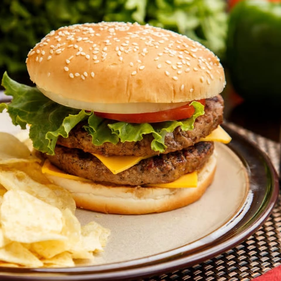 A double cheeseburger with lettuce, tomato, and onion, served with potato chips on a plate.