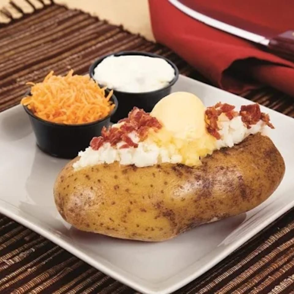 A loaded baked potato with butter, bacon bits, and sour cream, with shredded cheese on the side.